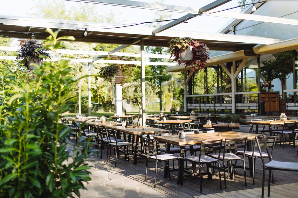 Covered summer terrace of a restaurant with wooden tables, chairs, and flooring.