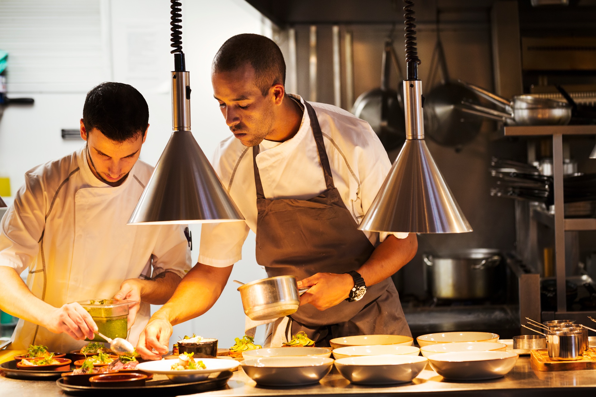 Two chefs standing in a restaurant kitchen, plating food.